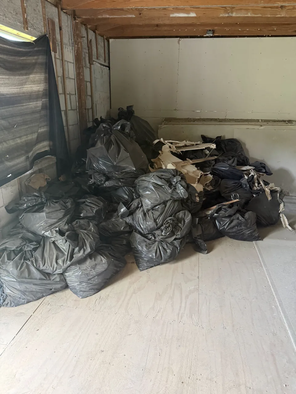 Room piled with black debris bags and drywall scraps