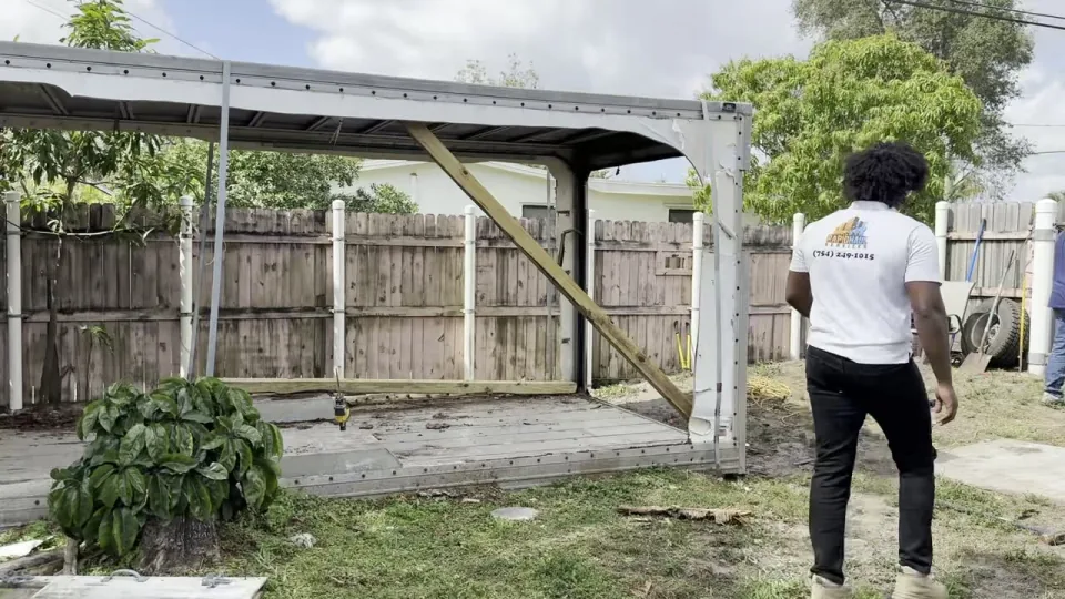 Rapid Haul crew member in a company shirt walks up to a backyard shed and carport about to be torn down