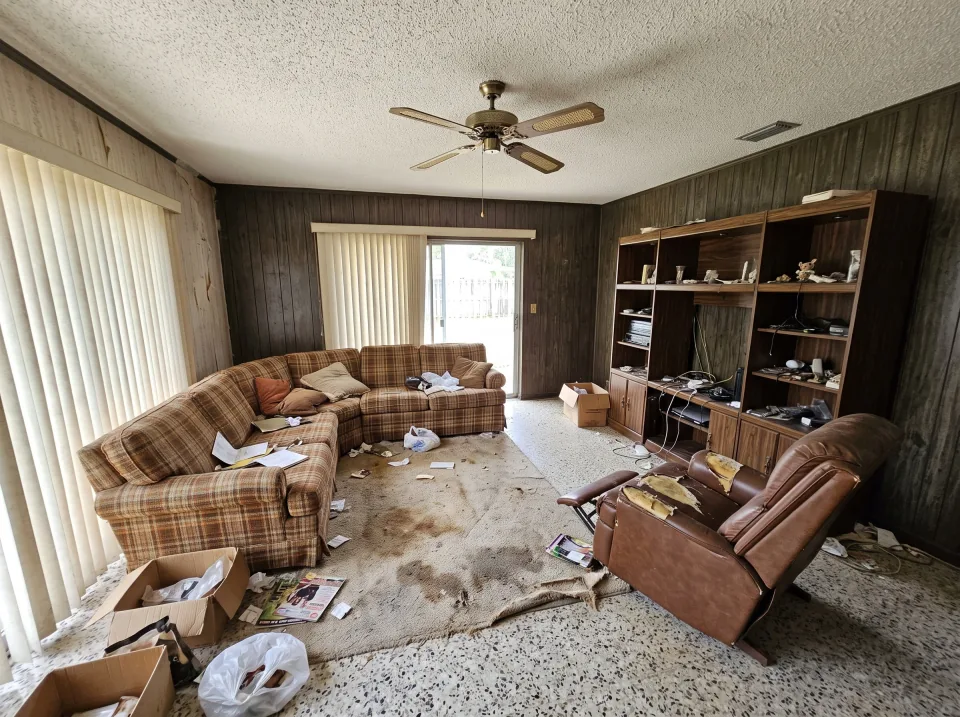 Illustration: a dated living room in a 1970s Florida house with terrazzo floors: a worn sectional sofa, a heavy wooden entertainment center, a broken recliner and a stained area rug.