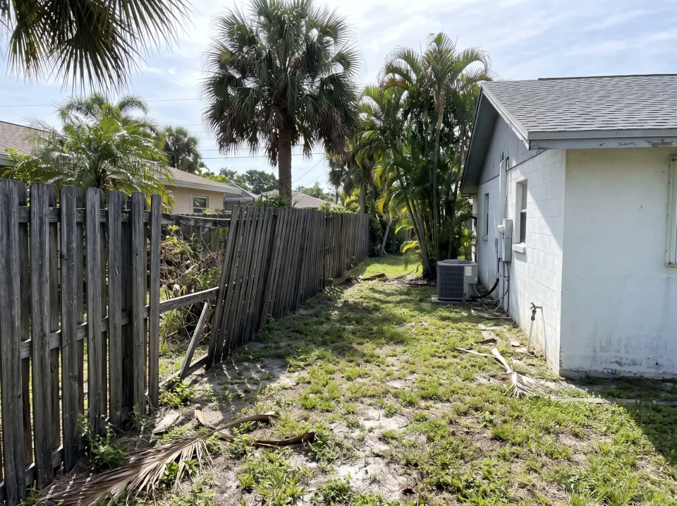 Illustration: a leaning, weathered wooden privacy fence with missing boards along the side yard at a white single-story Glen Ridge concrete block home with a gray shingle roof and palm trees, bright morning light