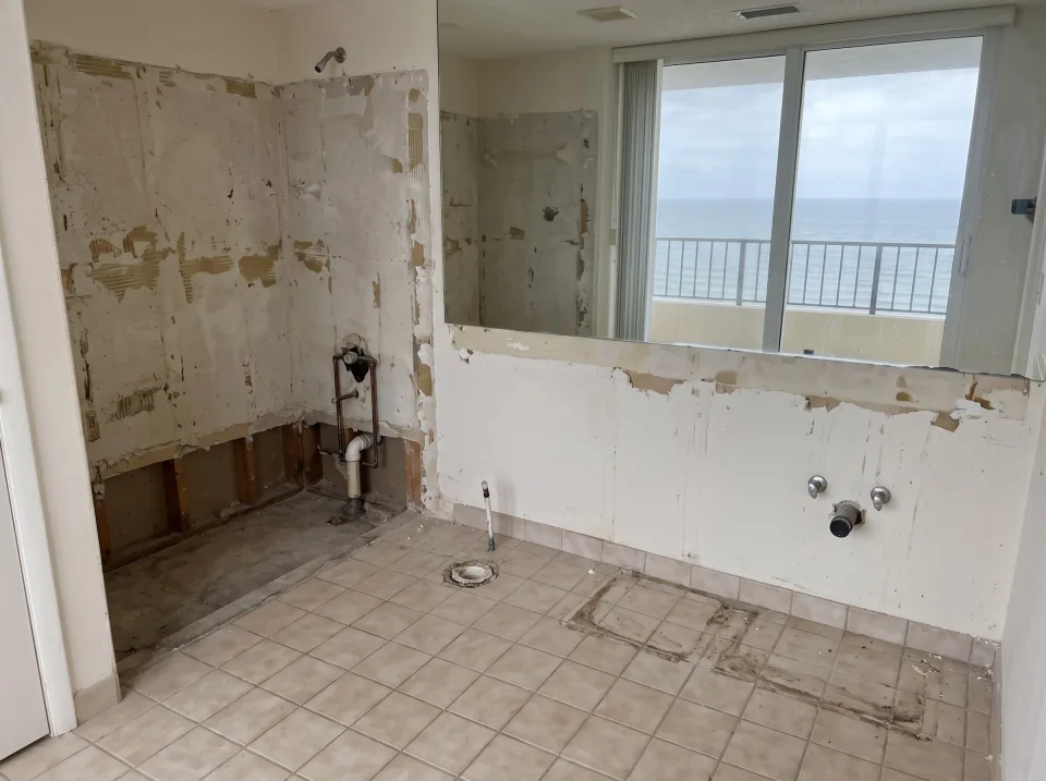 Illustration, after: the tile, tub, toilet and vanity removed, with bare walls, capped plumbing, a swept floor and the window visible
