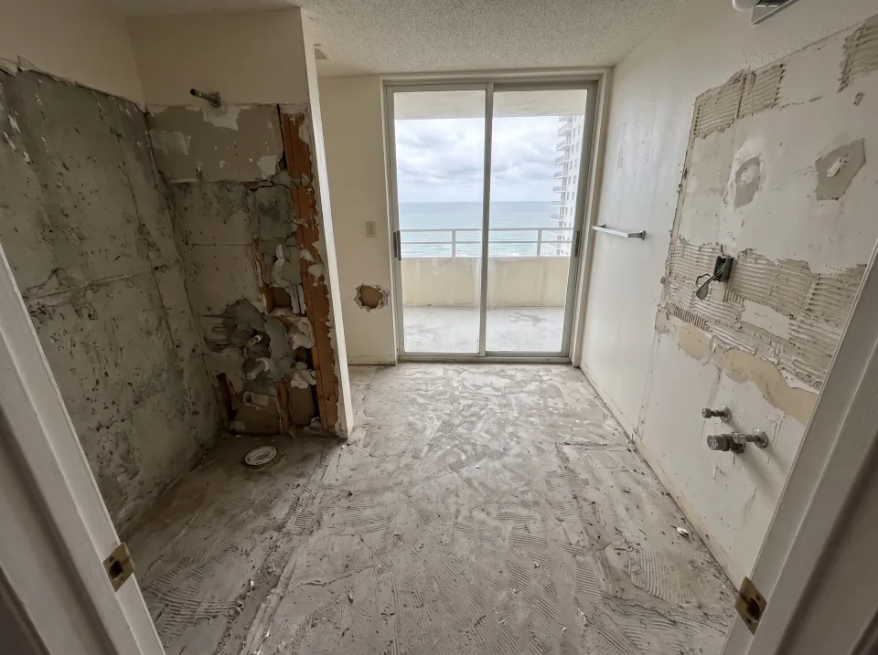 Illustration, after: the tile, tub, toilet and vanity removed, with bare walls, capped plumbing, a swept floor and the window visible