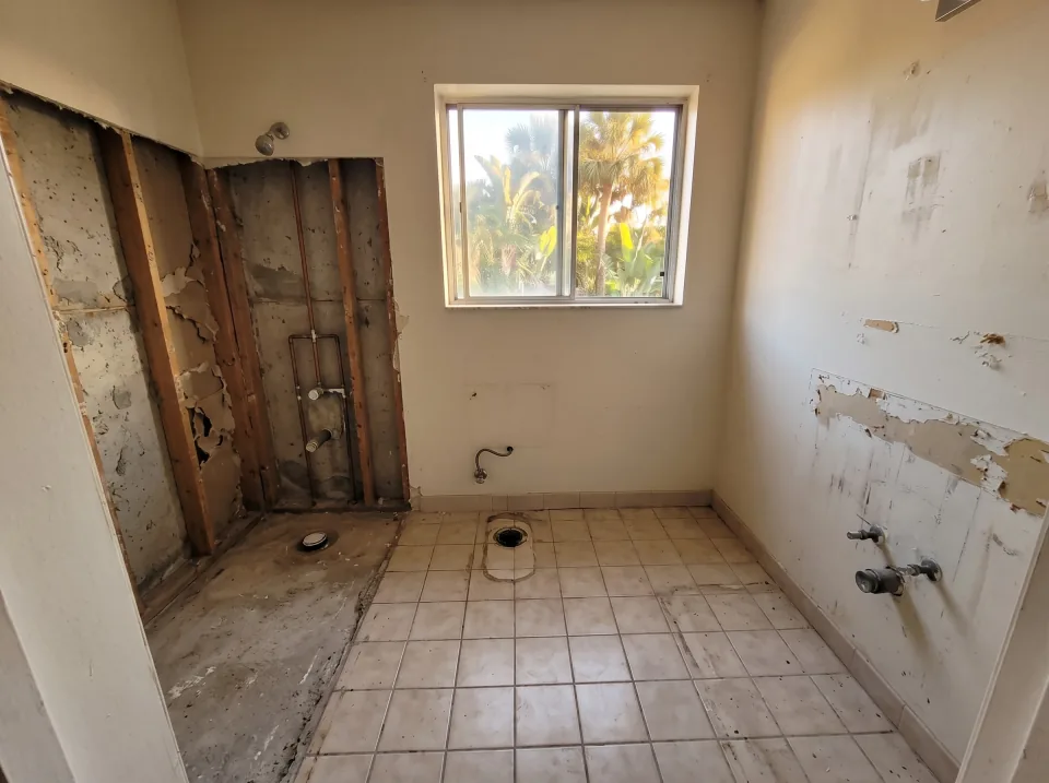 Illustration, after: the tile, tub, toilet and vanity removed, with bare walls, capped plumbing, a swept floor and the window visible
