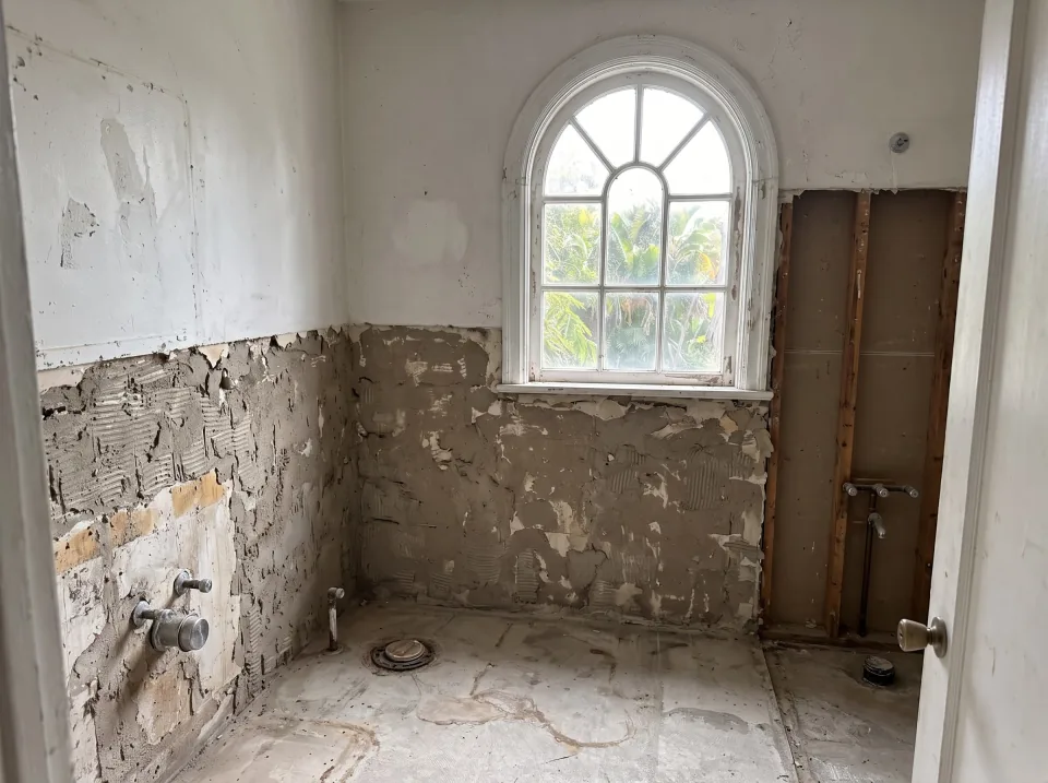 Illustration, after: the tile, tub, toilet and vanity removed, with bare walls, capped plumbing, a swept floor and the window visible