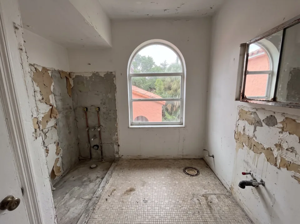 Illustration, after: the tile, tub, toilet and vanity removed, with bare walls, capped plumbing, a swept floor and the window visible