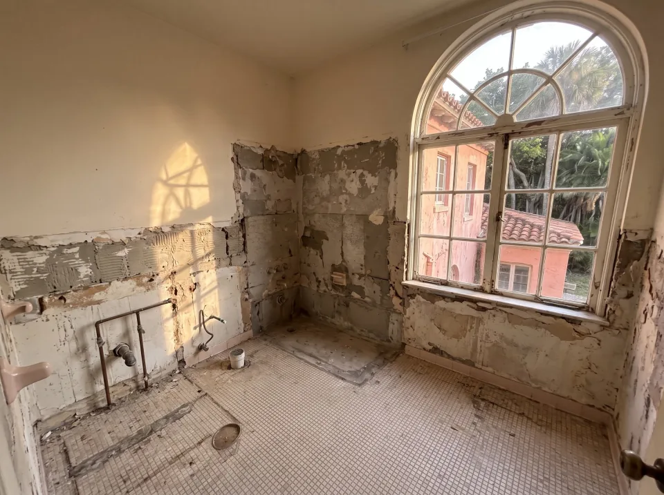 Illustration, after: the tile, tub, toilet and vanity removed, with bare walls, capped plumbing, a swept floor and the window visible