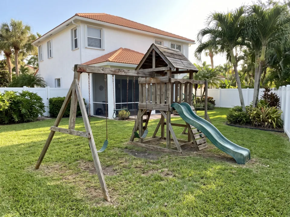 Illustration: a sun-faded wooden swing set and playhouse in the backyard at a white two-story home in a Tequesta gated community with manicured landscaping, barrel tile roof, bright morning light
