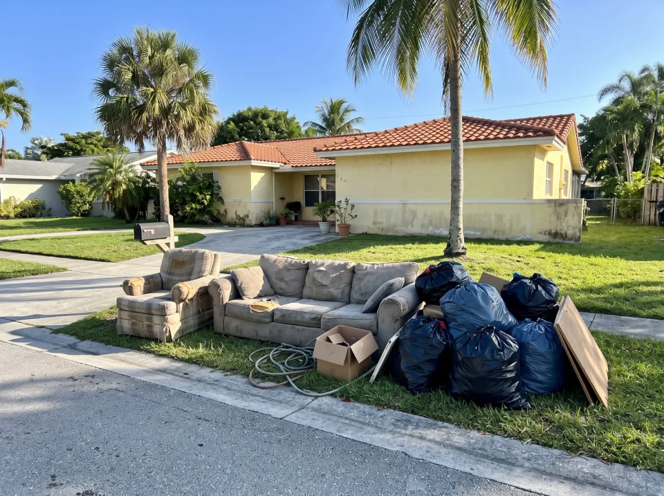 Illustration: a worn sectional sofa, an armchair and bagged junk piled at the curb at a pale yellow single-story Westchester concrete block home with a barrel tile roof and palm trees, bright morning light