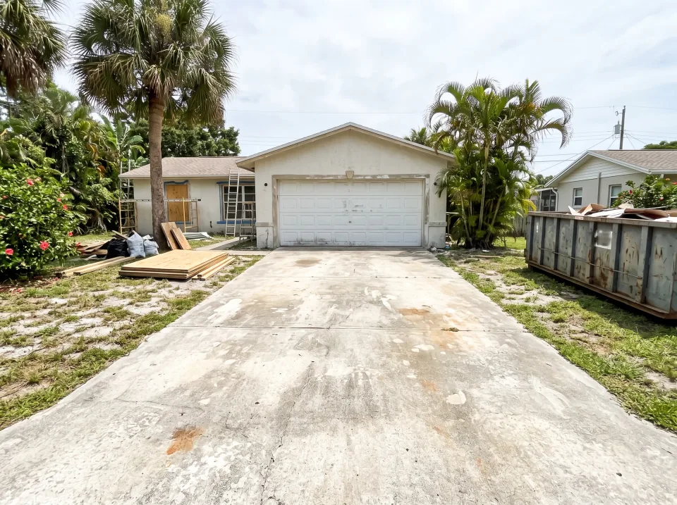 Illustration: an empty concrete driveway at a South Florida house under renovation, garage door closed.
