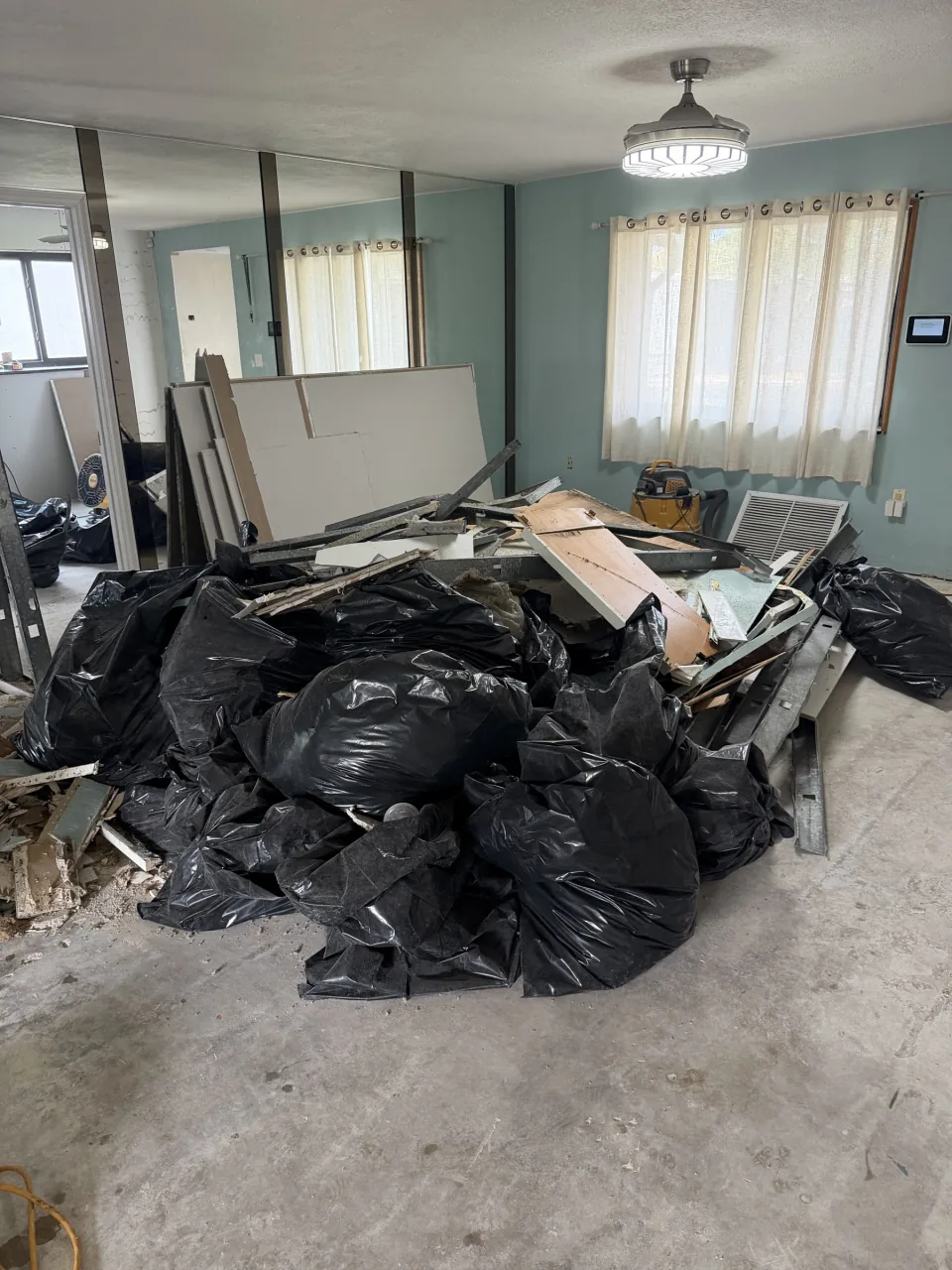 Contractor bags and drywall in a stripped room