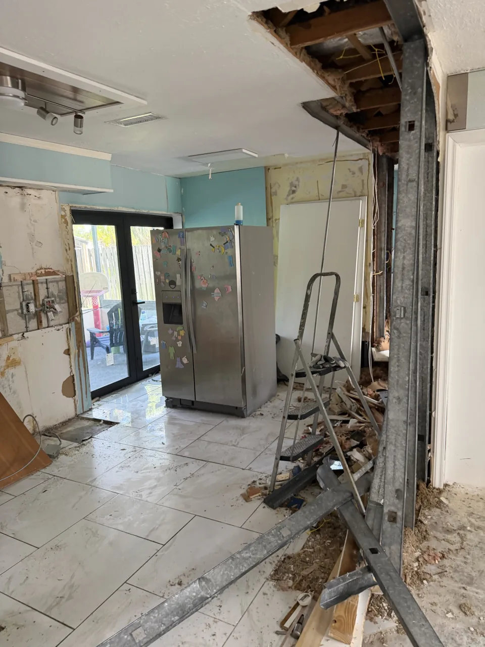 Same kitchen opened to the studs and ceiling framing, debris on the floor